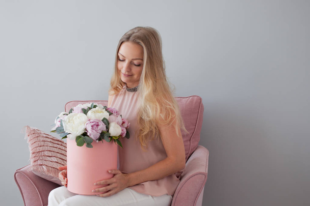Happy blonde woman with flowers in a hat box. Bouquet of peonies. Girl with a pink bouquet of peonies - Foto, Bild