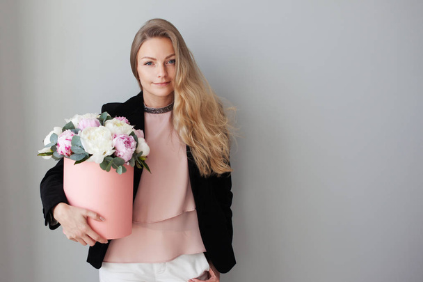 Charming blonde woman with flowers in a hat box. Bouquet of peonies. Girl in business style, receives flowers or gives - Photo, Image