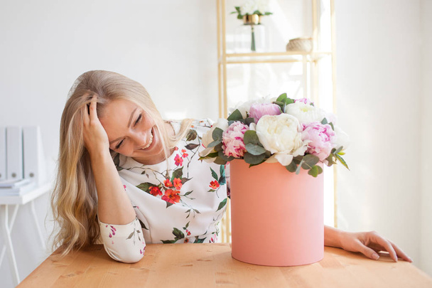 Happy blonde woman in a modern office with flowers in a hat box. Bouquet of peonies. - Valokuva, kuva