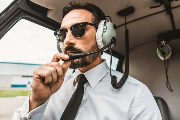 Confident pilot wearing sunglasses while sitting it the cabin - Zdjęcie, obraz