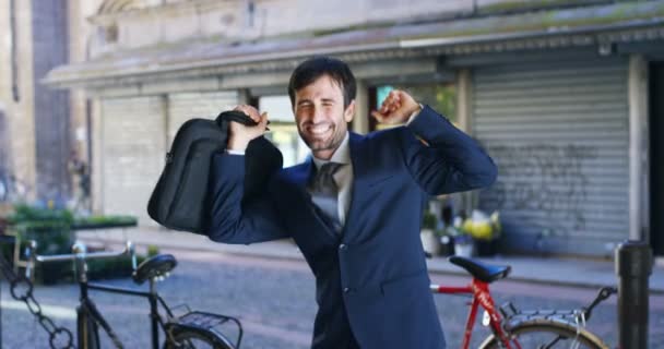 video of businessman dancing and celebrating success outdoors and holding case bag, street with bicycles on background  - Séquence, vidéo