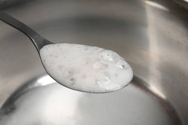 Chemical reaction of vinegar and baking soda in spoon over saucepan, closeup - Fotó, kép