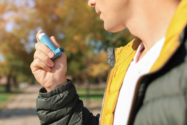Man using asthma inhaler outdoors. Health care - 写真・画像