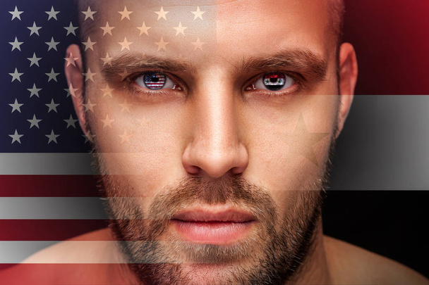 Portrait of a young serious man, in whose eyes the reflected national flag of Syria and America, against an isolated black background and flag - Photo, Image