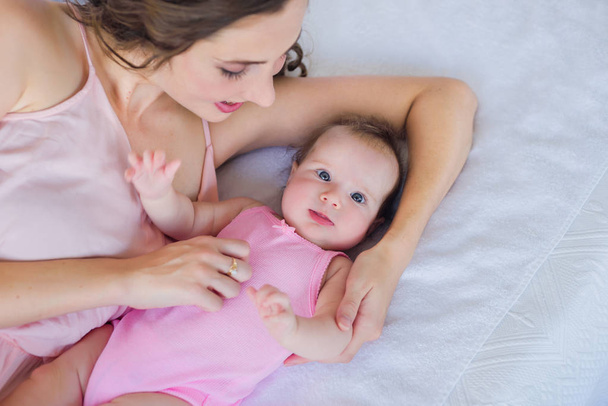 gyönyörű fiatal mamma cuddling 4 hónapos baba lány az ágyon - boldog anyaság koncepció - Fotó, kép