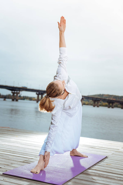 Young woman in triangle yoga pose near the water - Foto, Bild