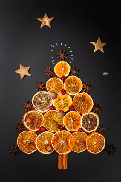 Kerstboom gemaakt van gedroogde sinaasappels, kaneel en steranijs op donkere achtergrond. Van boven gezien. Verticale compositie - Foto, afbeelding