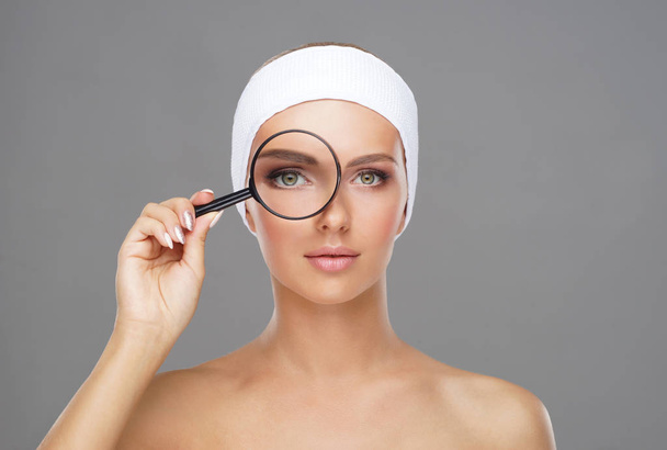 Face of young and beautiful girl and a magnifying glass. Plastic surgery, face lifting and aesthetic medicine concept. - Photo, Image
