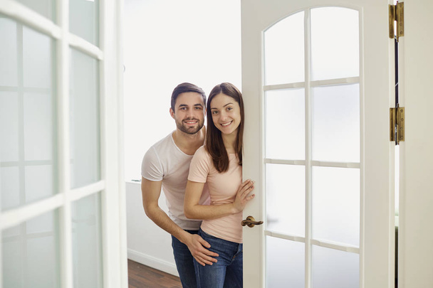 A couple with smiles opens the door to their house. - Foto, Bild
