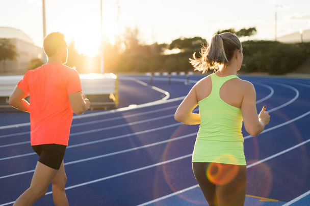 Couple of athletic runners running on a blue race track. Sport. - 写真・画像