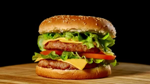 Friss étvágygerjesztő hamburger forog a fekete háttér. Problémamentes loopable lövés, 4k. - Felvétel, videó