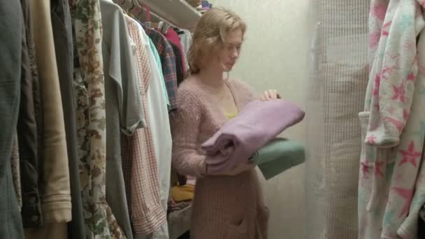Hermosa chica sonríe y va sobre toallas en el estante en su vestidor
 - Imágenes, Vídeo