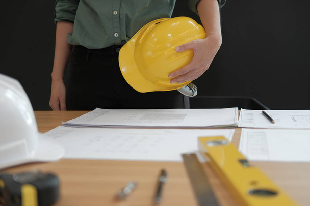 engineer architect worker holding safety helmet hardhat wtih construction blueprint on desk at workplace - Photo, Image