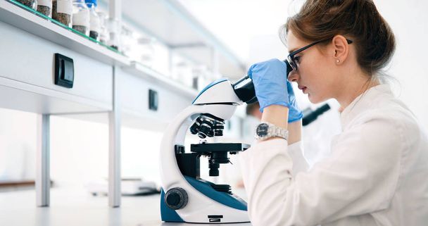 Young female scientist looking through microscope in laboratory - Foto, Bild