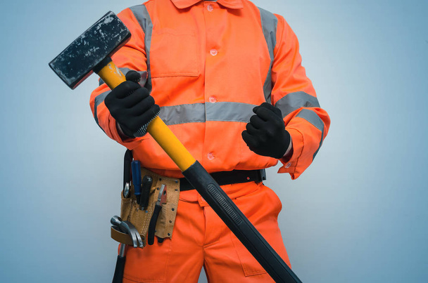 Builder worker holding in hands a big sledgehammer isolated on blue background. Under construction concept. - Φωτογραφία, εικόνα