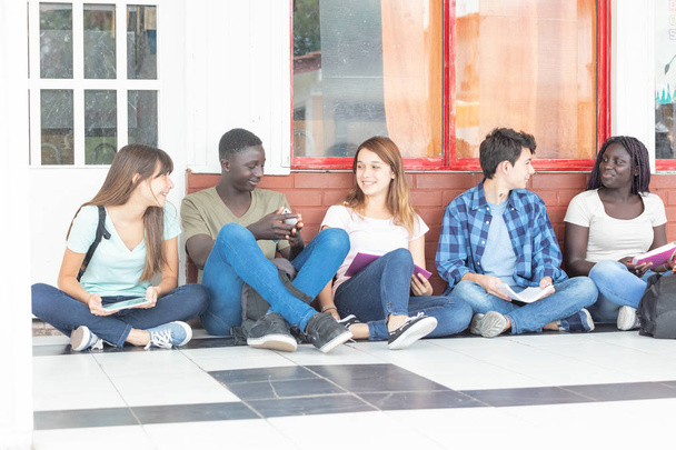 Groupe d'adolescents multi-ethniques assis dans le couloir, se parlant
. - Photo, image