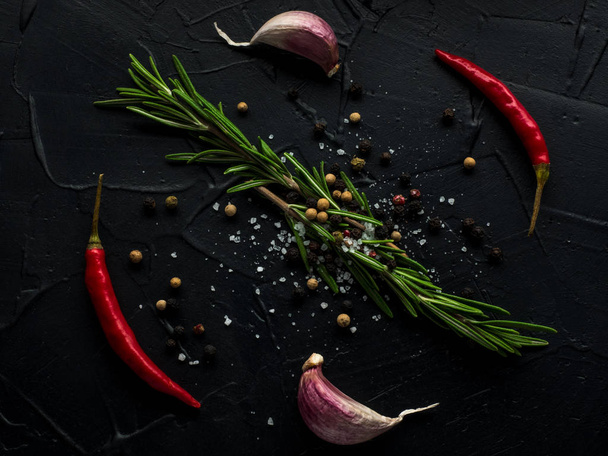 Red hot chilli pepper, garlic and rosemary with sea salt and colored pepper on black background - Foto, afbeelding