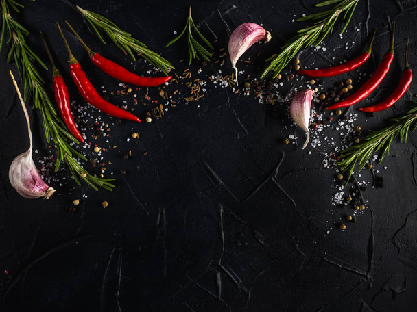 rote Chilischote, Knoblauch und Rosmarin mit Meersalz und farbigem Pfeffer auf schwarzem Hintergrund - Foto, Bild