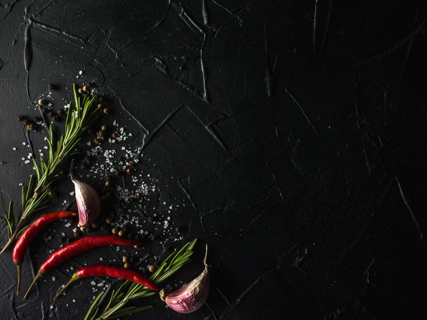Rode peper peper, knoflook en rozemarijn met zeezout en gekleurde peper op zwarte achtergrond - Foto, afbeelding