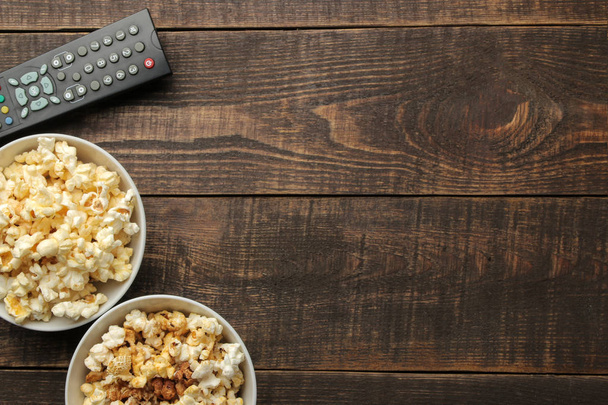 Popcorn und Fernbedienung auf braunem Holzhintergrund. Konzept des Kinobesuchens zu Hause. Draufsicht mit Platz für Text - Foto, Bild