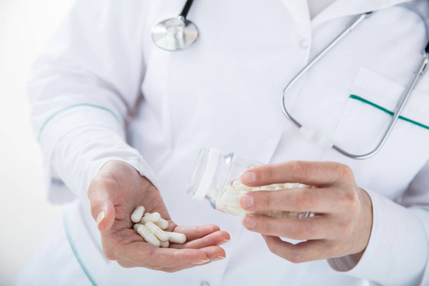 Dottore su sfondo bianco versa pillole dal barattolo alla mano. Vista orizzontale
 - Foto, immagini
