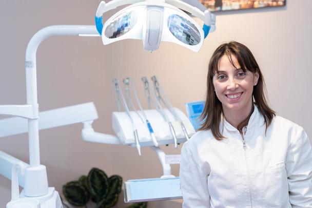 Jonge en professionele tandarts glimlacht in haar nieuwe tandartspraktijk. - Foto, afbeelding