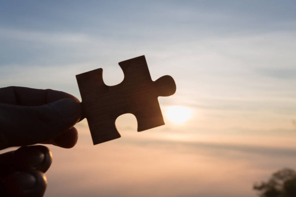Silueta de mano sosteniendo Jigsaw con fondo Sunrise. .. símbolo de asociación y conexión. estrategia empresarial. - Foto, Imagen