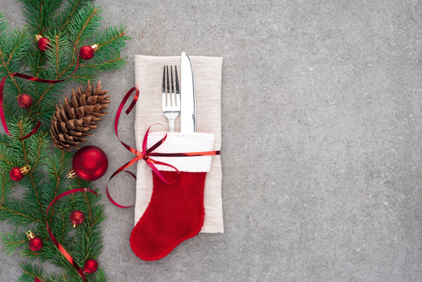 näkymä ylhäältä haarukan ja veitsen santa sukka kääritty punainen nauha pöydälle männynkäpy ja haara koristeltu joulupallot
  - Valokuva, kuva