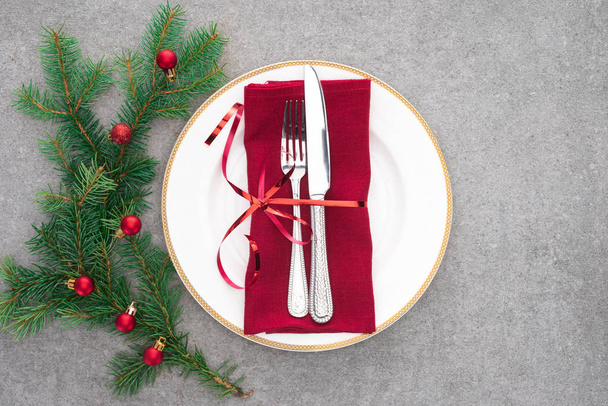 вид сверху сервированного стола с тарелкой, вилкой и ножом, завернутым праздничной лентой рядом с веткой, украшенной рождественскими шарами
  - Фото, изображение