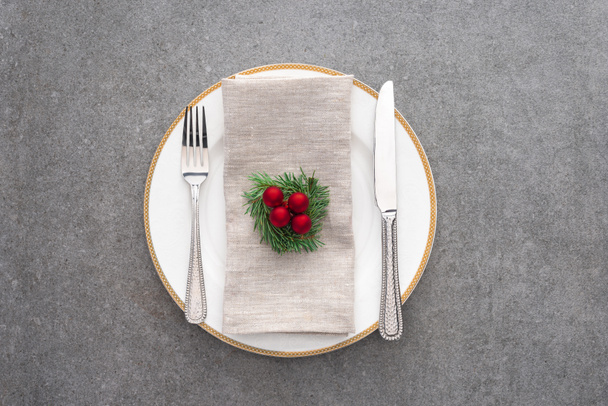 top view of served plate with fork, knife and decorated evergreen branch with christmas balls on grey surface - Photo, image