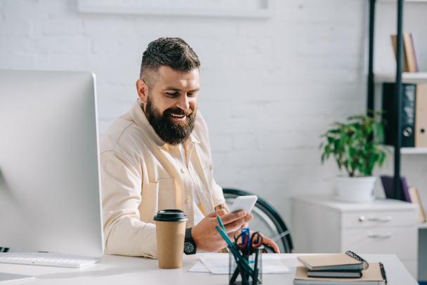 Smějící se podnikatel sedí v kanceláři a při pohledu na smartphone - Fotografie, Obrázek