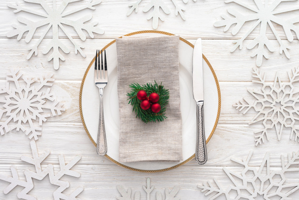 bovenaanzicht van de plaat met vork, mes en evergreen tak met kerstballen, omgeven door versierde sneeuwvlokken  - Foto, afbeelding