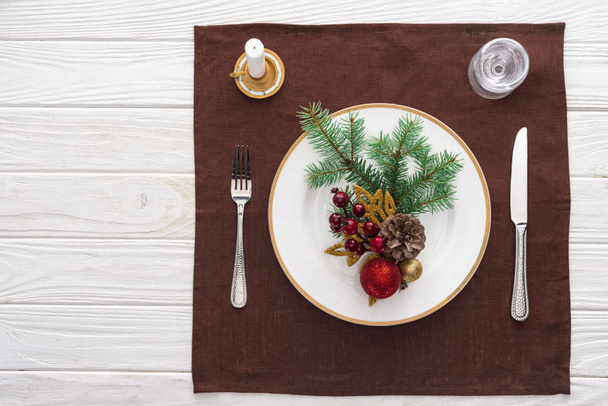 top view of served table with  wine glass, plate, fork, knife, spoon, candle and christmas decorations on tablecloth  - Fotografie, Obrázek
