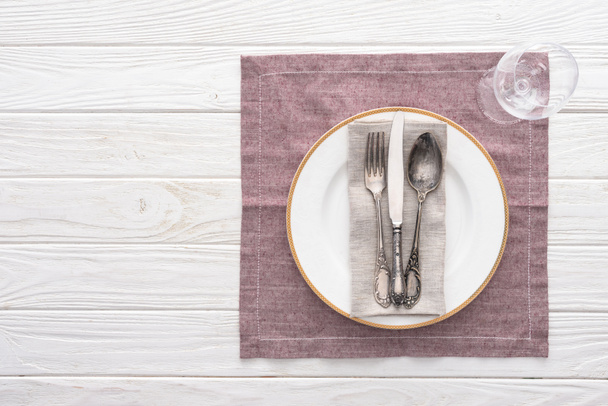 Плоский лежал с тарелкой, вилкой, ножом, ложкой возле бокала вина на подаваемом столе со скатертью
 - Фото, изображение