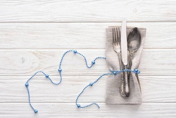 view from above of fork, knife and spoon wrapped by decorative blue beads on wooden table - Photo, Image