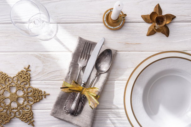 ワイングラス、ゴールデン クリスマス ボール、キャンドル、フォーク、スプーン、ナイフの木製のテーブルにリボンで包まれた板の上から見る  - 写真・画像