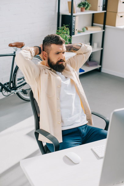 Bearded businessman sitting in office chair and putting hands behind head - Foto, immagini
