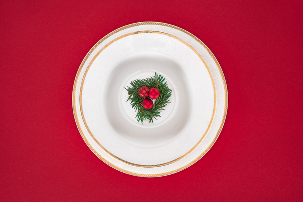 flat lay with evergreen tree branch with decorated christmas balls on plate isolated on red - Foto, immagini
