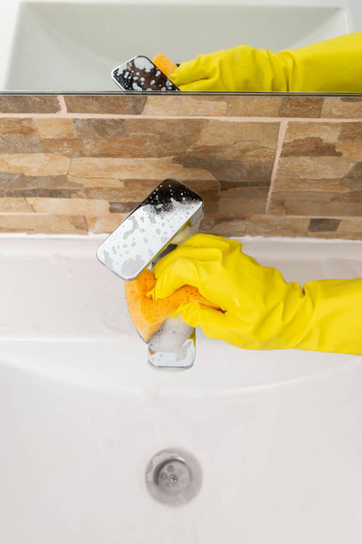 Grifo de agua Inox que se limpia con esponja y espuma por persona con guantes de goma higiénicos amarillos
 - Foto, Imagen