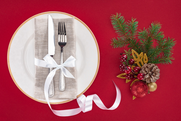 elevated view of fork and knife wrapped by ribbon on plate near christmas decorations isolated on red - Foto, Imagem