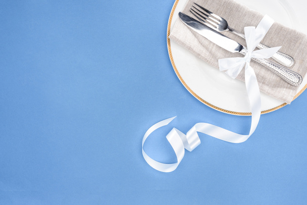 elevated view of fork and knife wrapped by festive ribbon on plate isolated on blue - Photo, Image