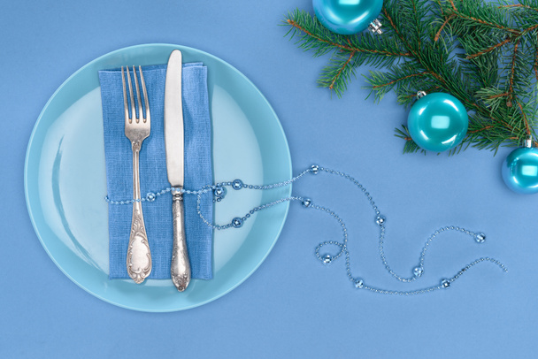 vue de dessus de la fourchette et du couteau enveloppés par des perles sur l'assiette près des branches persistantes avec des boules de Noël isolées sur bleu
 - Photo, image