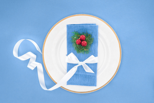 top view of plate with christmas balls and napkin wrapped by festive ribbon isolated on blue  - Foto, Bild