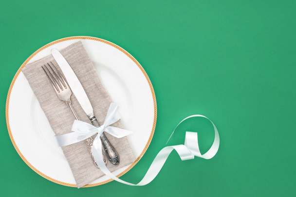 elevated view of plate with fork and knife wrapped by festive ribbon isolated on green - Zdjęcie, obraz