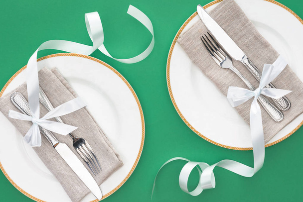 flat lay with forks and knives wrapped by festive ribbons on plates isolated on green - Foto, imagen