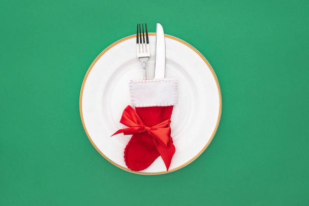 top view of fork and knife in christmas sock on plate isolated on green - Valokuva, kuva