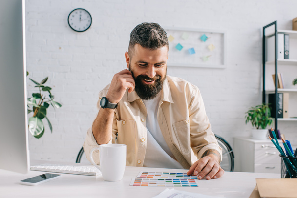 Мужской дизайнер сидит и смотрит на цветовую палитру в офисе
  - Фото, изображение