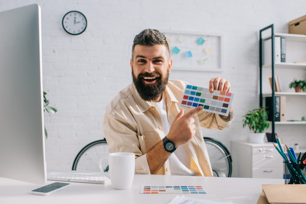Designer barbudo gesticulando na paleta de cores no escritório moderno
 - Foto, Imagem