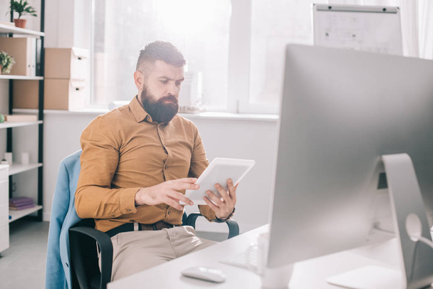 focused adult business man sitting at office desk and using digital tablet at workplace - Foto, Imagem