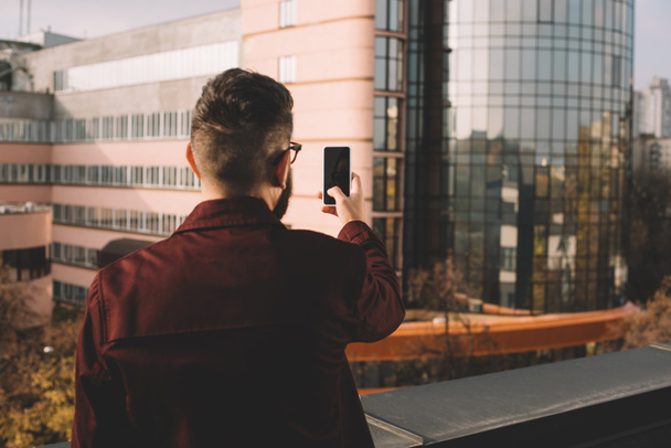 rear view of adult man taking selfie on rooftop with beautiful view - Photo, Image